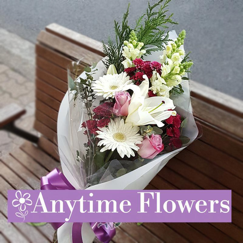 A beautifully arranged bouquet of white lilies, pink roses, white gerberas, and red carnations, tied with a purple ribbon.