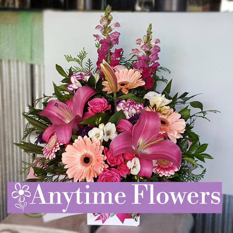 A vibrant bouquet featuring pink lilies, peach gerberas, and roses, accented with lush greenery.