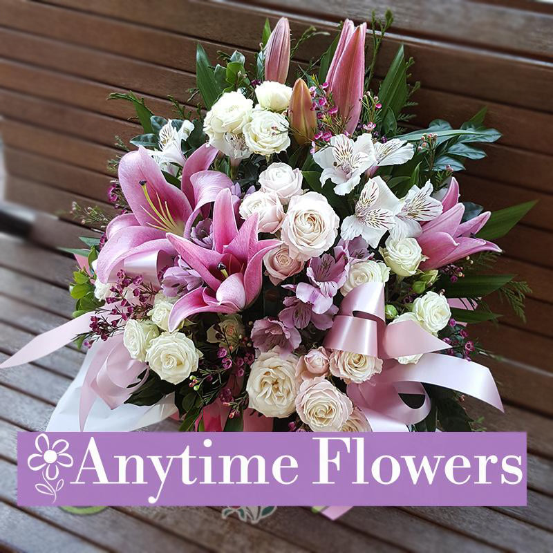 A delicate bouquet of pink lilies, white roses, and wax flowers, accented with greenery and tied with a satin ribbon.