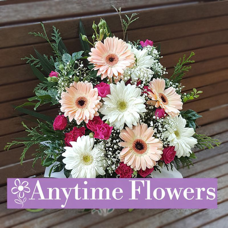 A bouquet featuring soft peach and white gerberas, pink roses, and baby's breath with lush greenery.
