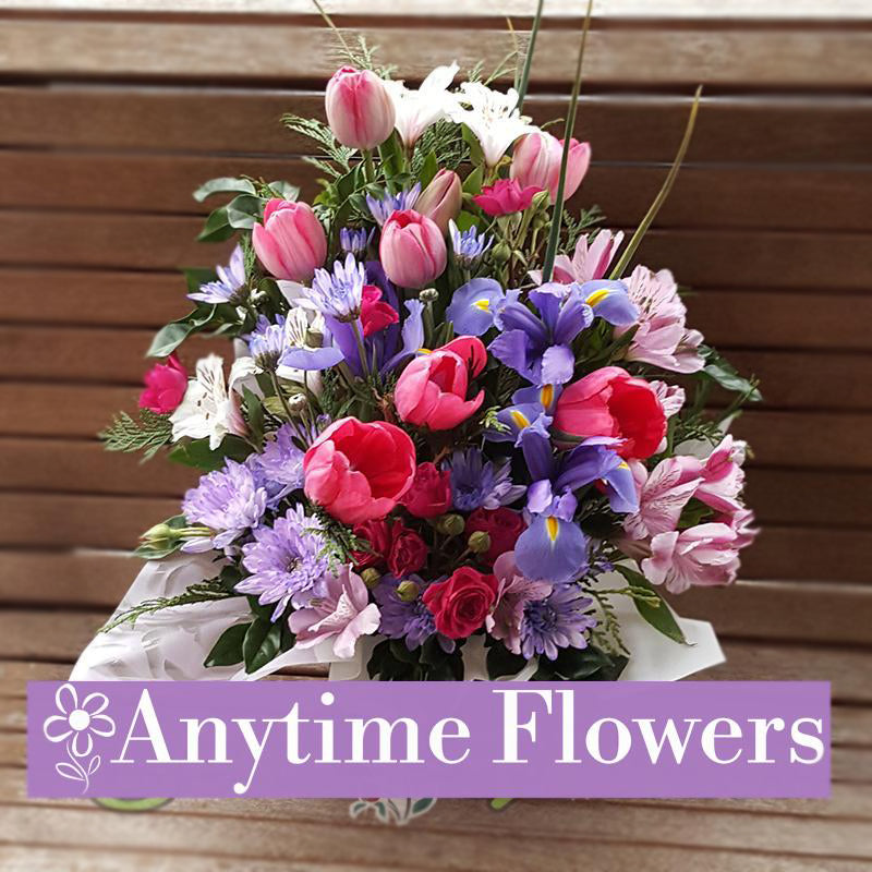 A cheerful bouquet of tulips, purple irises, and seasonal flowers, accented with fresh greenery.
