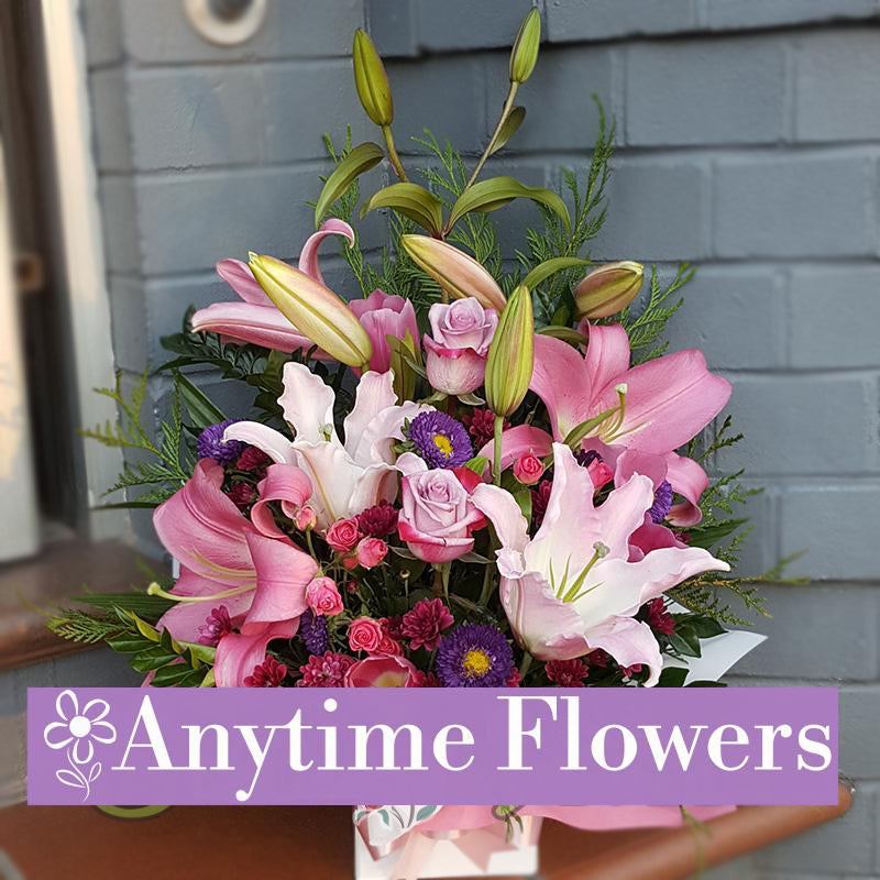 A beautiful box arrangement featuring pink lilies, roses, and purple asters, accented with fresh greenery for an elegant and charming design.