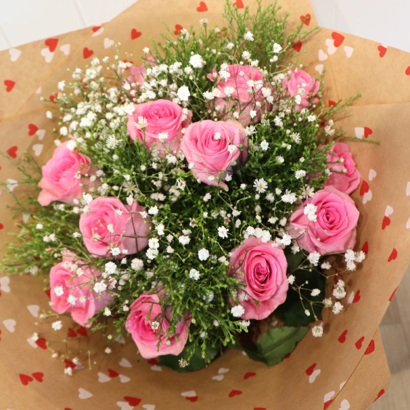 A sophisticated floral bouquet arrangement with lush pink roses, elegantly wrapped in a premium black gift wrap.