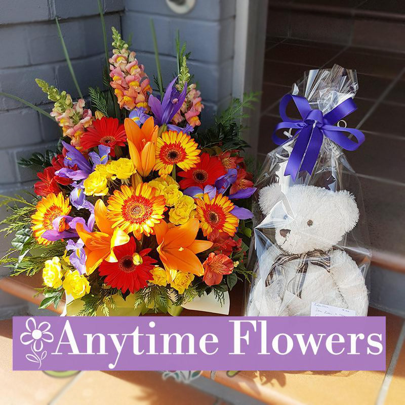 A vibrant bouquet of orange lilies, yellow and red gerberas, and purple irises, paired with a gift-wrapped teddy bear for a joyful celebration set.