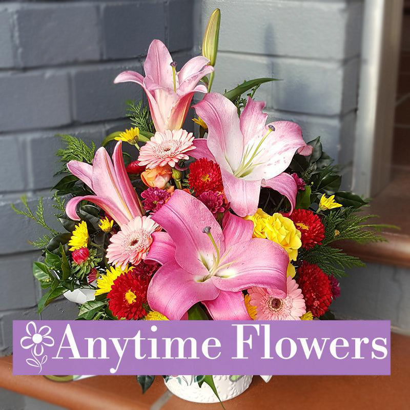 A stunning bouquet featuring pink lilies, yellow gerberas, pink gerberas, and red chrysanthemums, arranged and accented with lush greenery.