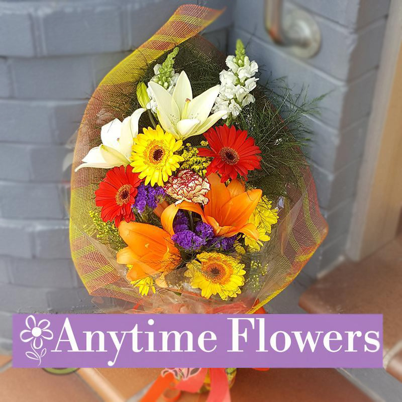 A vibrant bouquet featuring orange lilies, yellow and red gerberas, white lilies, purple statice, and lush greenery for a bold design.
