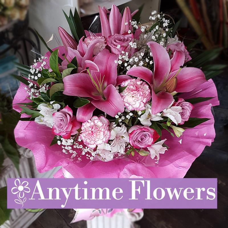A luxurious bouquet featuring pink lilies, roses, and carnations, accented with baby's breath and fresh greenery, wrapped in blush-toned fabric with a satin ribbon.