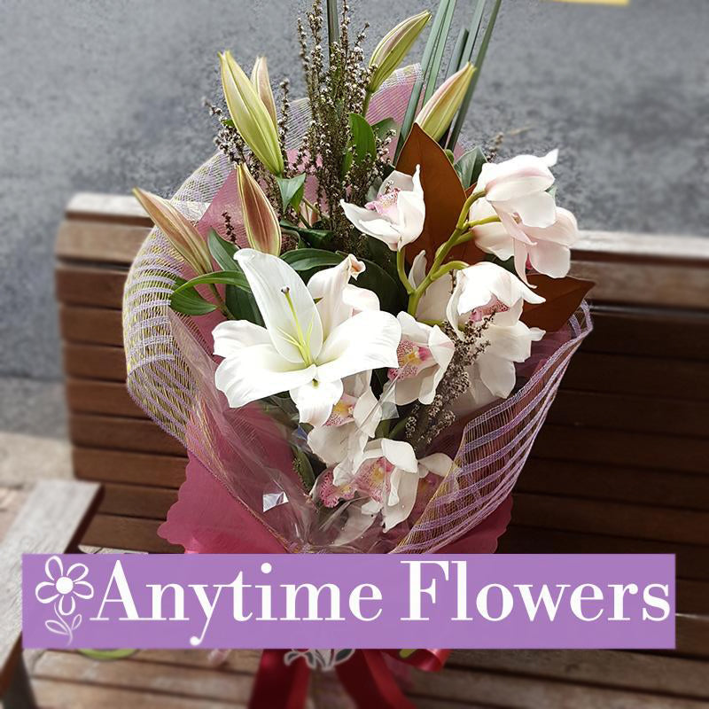 A luxurious bouquet featuring pristine white lilies and blush pink orchids, elegantly wrapped in blush-toned mesh with a satin ribbon, perfect for a refined and sophisticated floral gift.