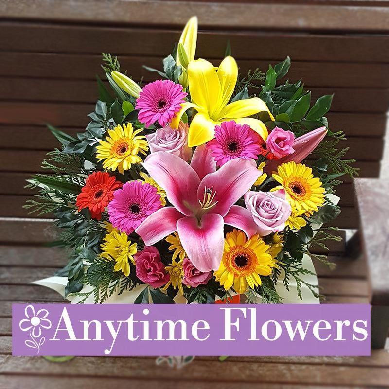 A radiant bouquet featuring pink lilies, yellow gerberas, pink gerberas, and purple roses, accented with lush greenery for a cheerful design.