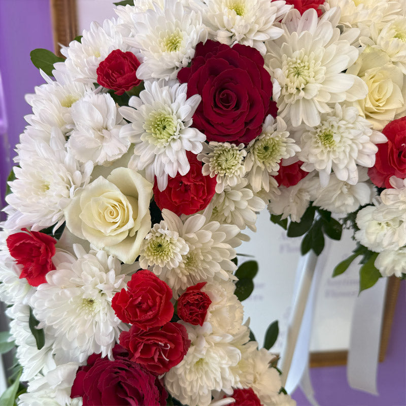 A detailed close-up of an elegant heart-shaped sympathy wreath with soft white and bold red florals, accented with delicate greenery.