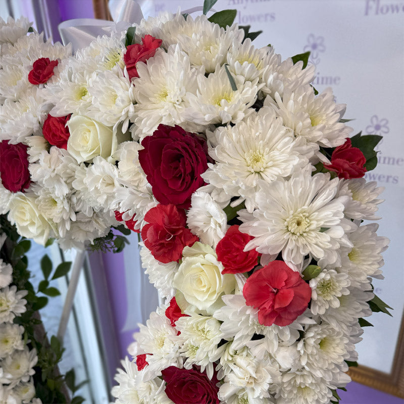 A beautifully arranged funeral wreath in a heart shape, showcasing a balanced mix of white blooms and red accents on a display stand.