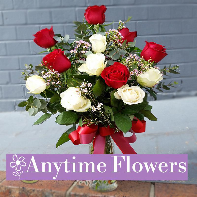 A romantic arrangement of red and white roses with pink filler flowers and lush greenery.