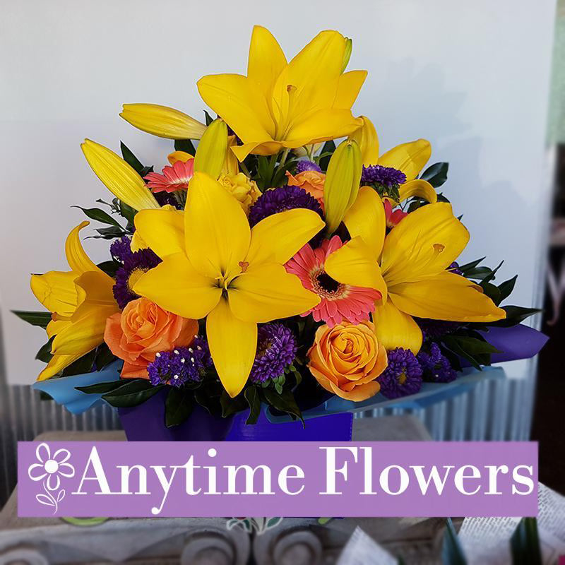 A vibrant bouquet of yellow lilies, orange roses, and purple asters with lush greenery.
