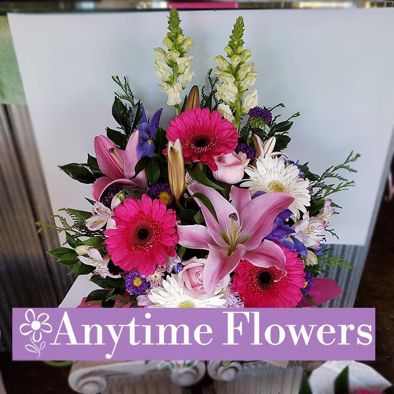 A delightful arrangement of pink gerberas, lilies, white daisies, and purple irises with lush greenery.