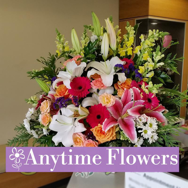 A grand display of white lilies, orange roses, pink gerberas, and yellow snapdragons with lush greenery.