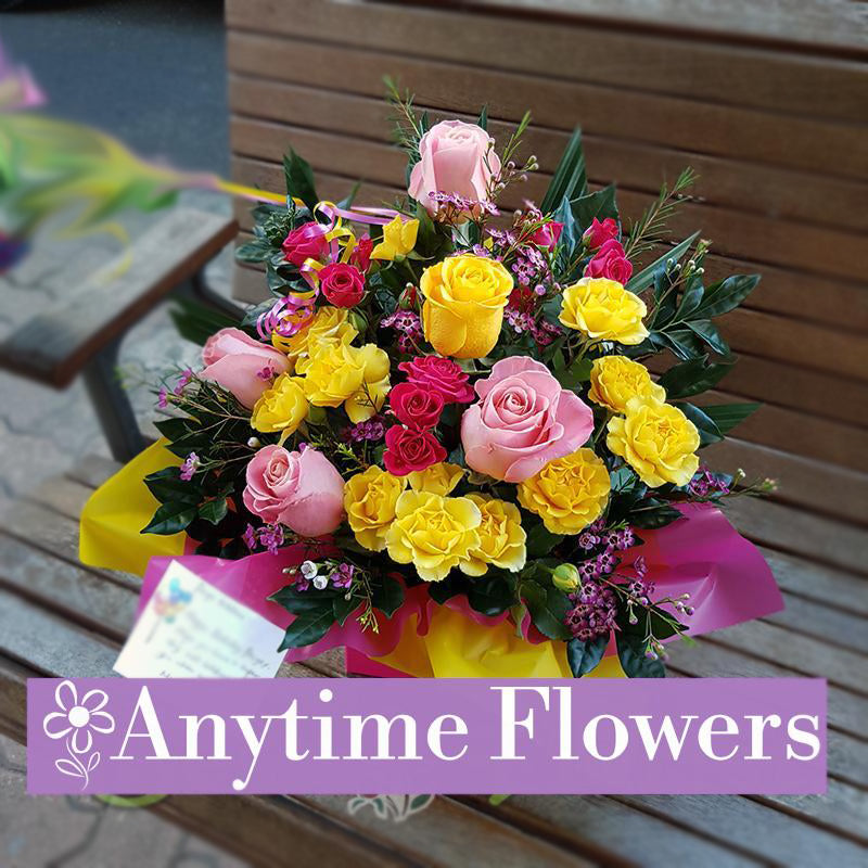A romantic arrangement of pink roses, yellow carnations, and red spray roses with lush greenery.