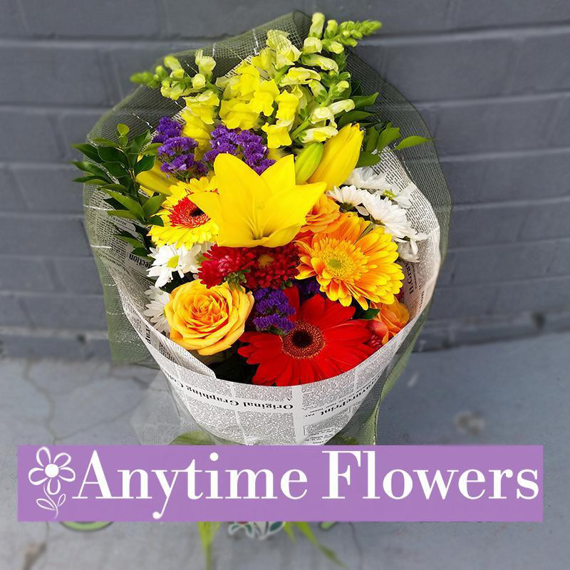 A cheerful bouquet of yellow lilies, orange gerberas, and white daisies with rustic wrapping.