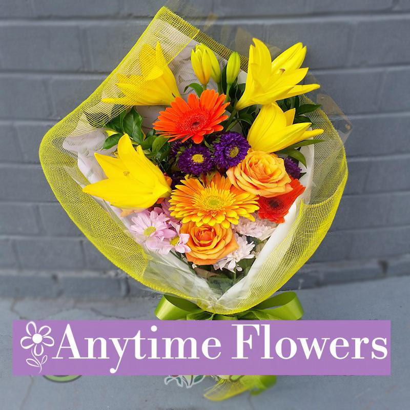 A vibrant bouquet of yellow lilies, orange gerberas, and purple blooms wrapped in yellow mesh.