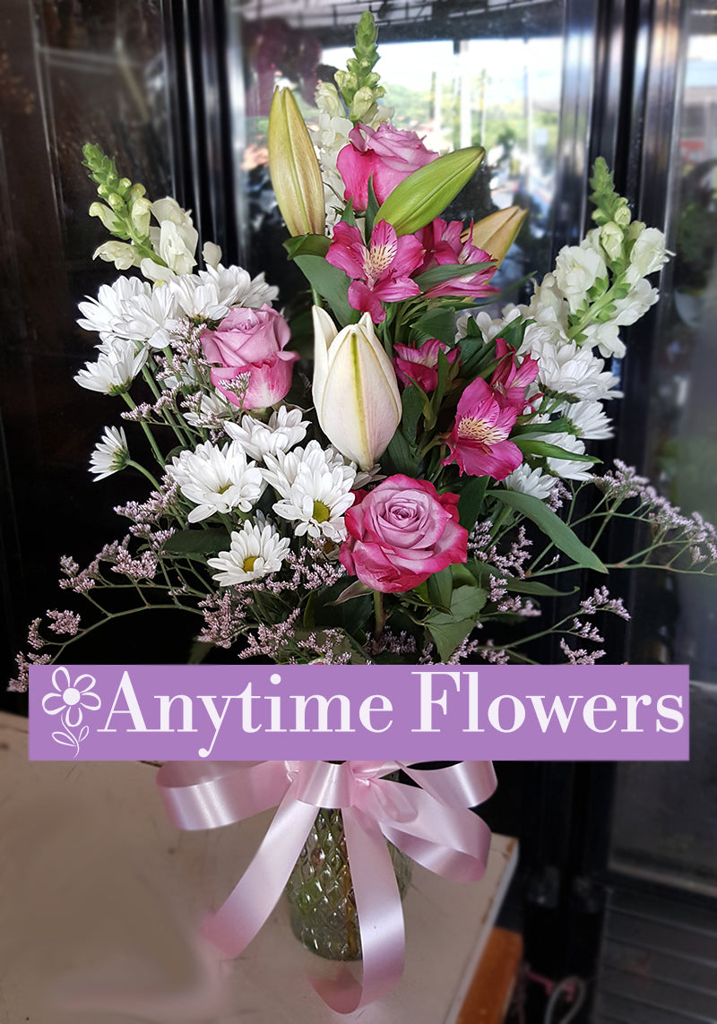 Charming bouquet of pink roses, pink lilies, and white daisies in a vase with a lavender ribbon.