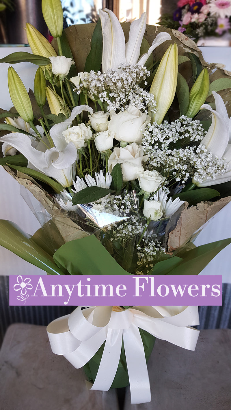 Elegant bouquet with white lilies, roses, and baby's breath wrapped in white ribbon.