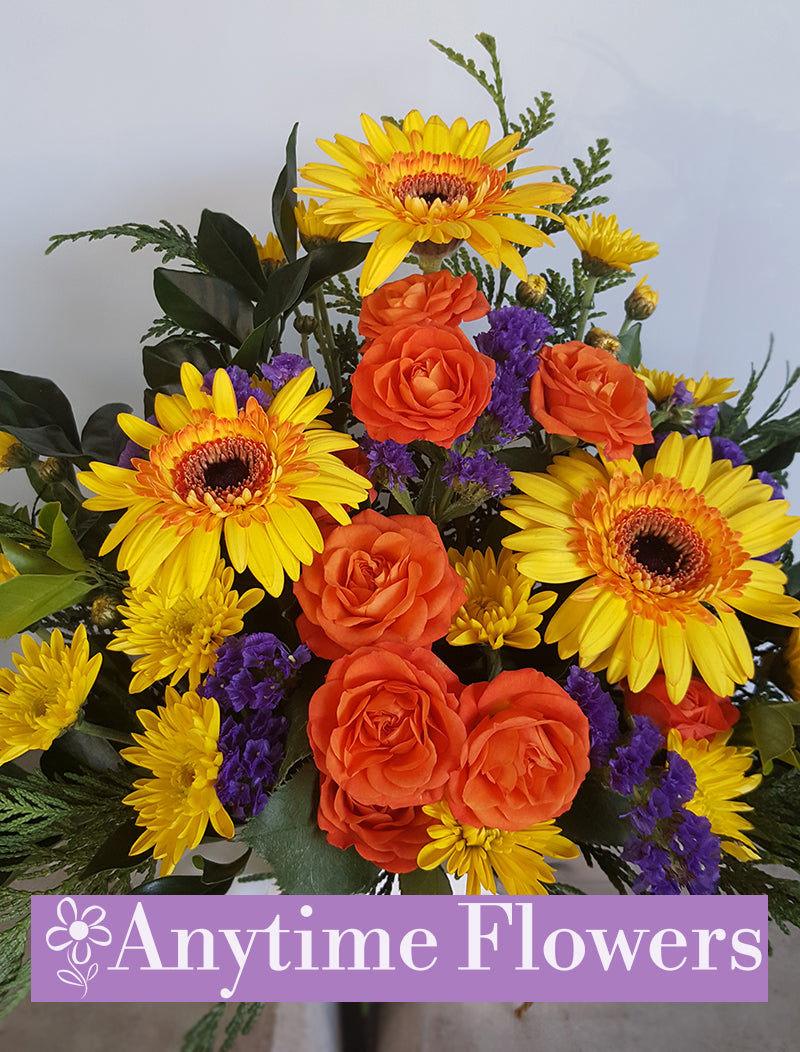 Vivid bouquet of orange roses, yellow gerberas, and purple accents.