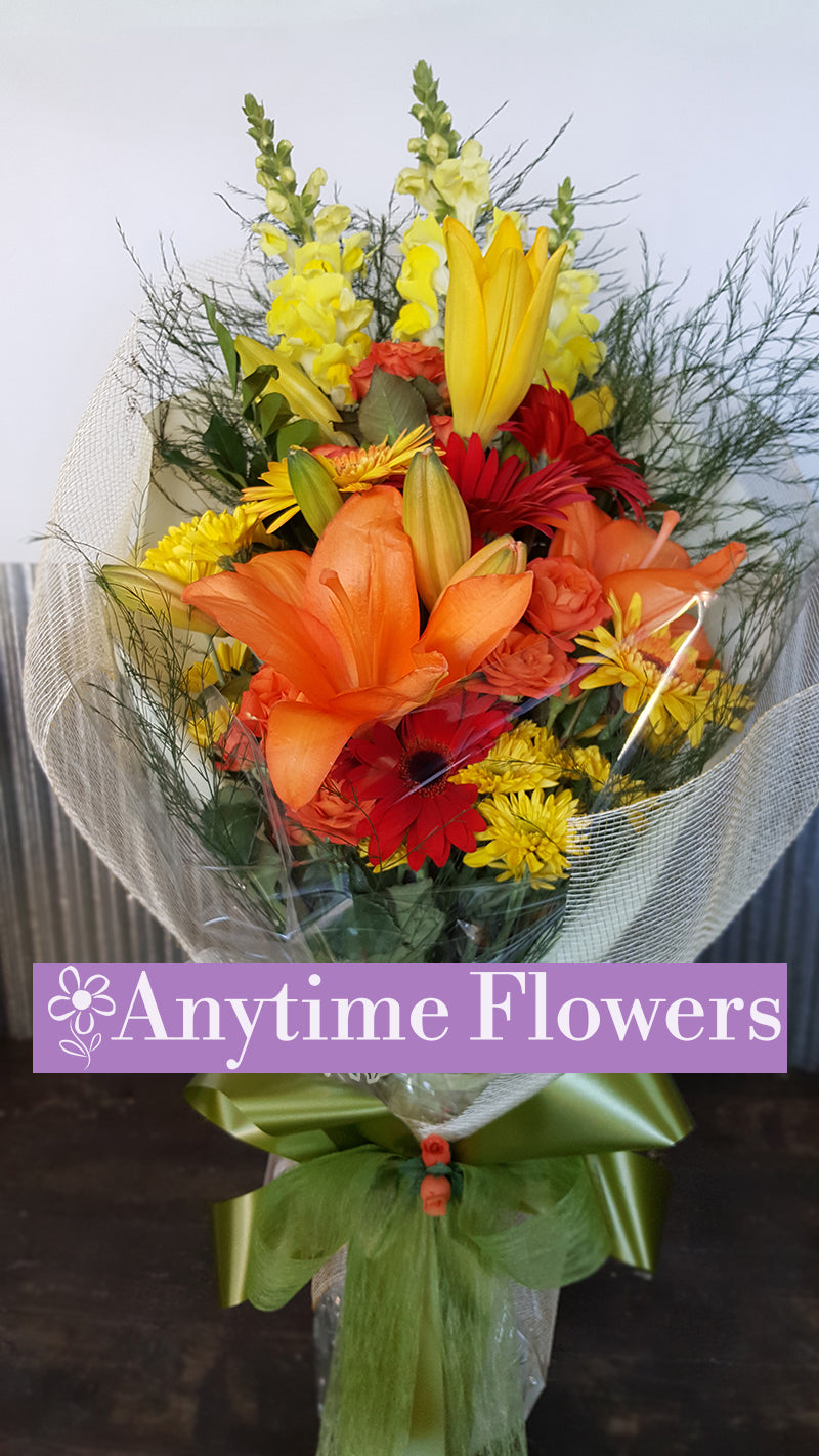 Bright bouquet with orange lilies, red gerberas, and yellow snapdragons wrapped in mesh.
