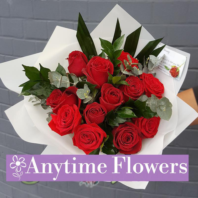 Romantic bouquet of red roses accented with lush greenery in white wrap.