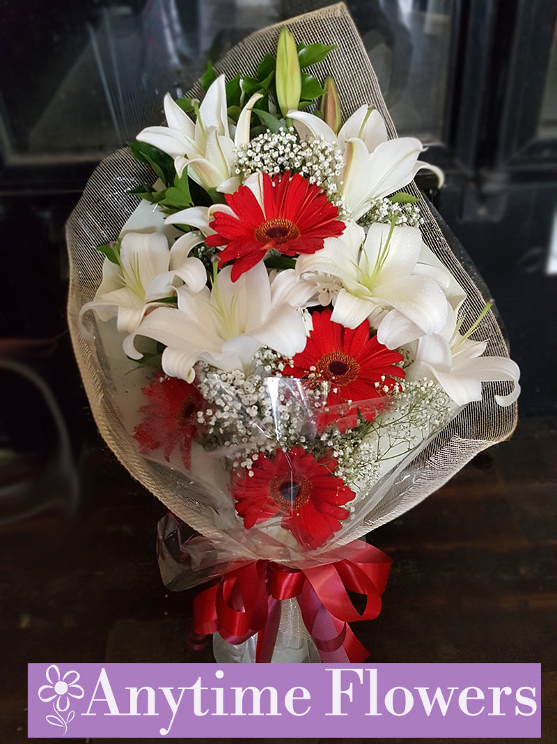 A bouquet of red gerberas, white lilies, and baby's breath.