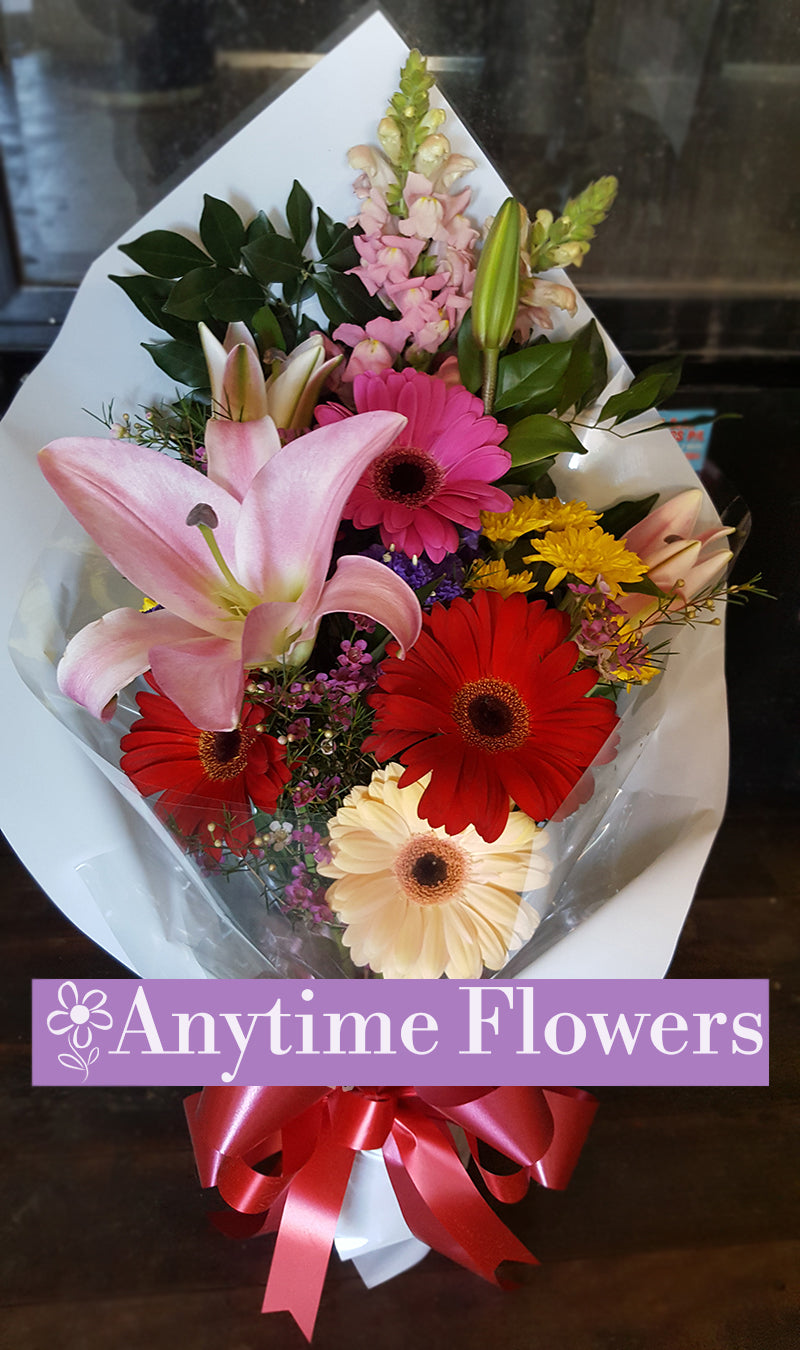 A pastel bouquet with pink lilies, red and white gerberas, and lush greenery.
