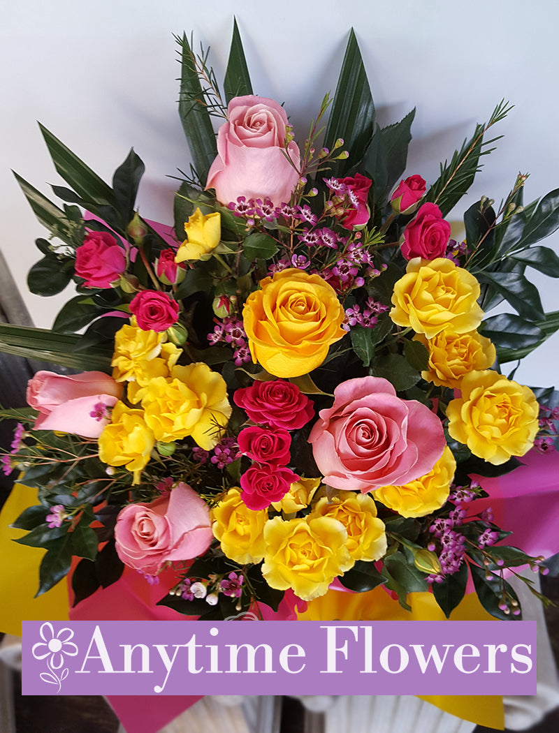 A cheerful bouquet of pink, yellow, and red roses with seasonal greens.
