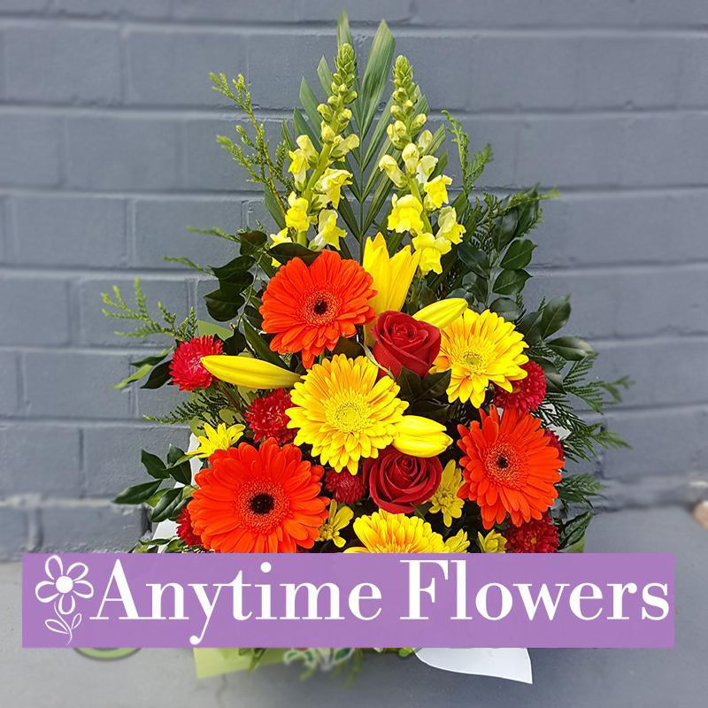 A warm arrangement of orange gerberas, yellow lilies, and red roses.