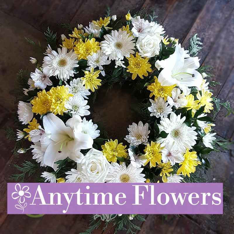 A circular floral wreath with white lilies, yellow chrysanthemums, and white roses.