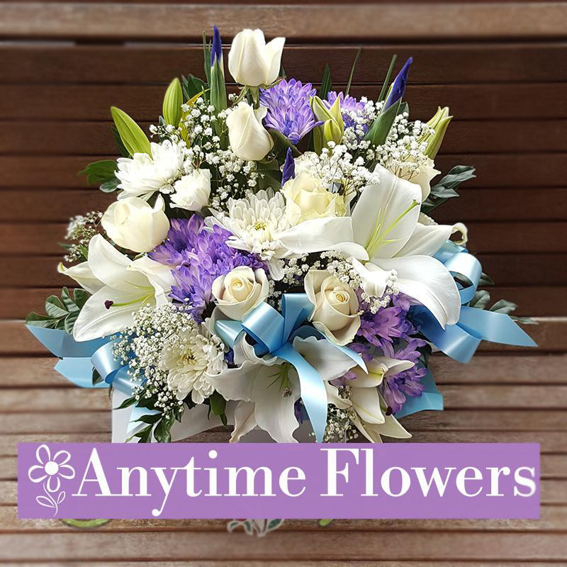 A serene bouquet of white lilies, roses, and chrysanthemums with soft blue accents.