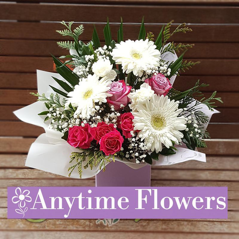 A bouquet of white gerberas, pink roses, and baby's breath with lush greenery.