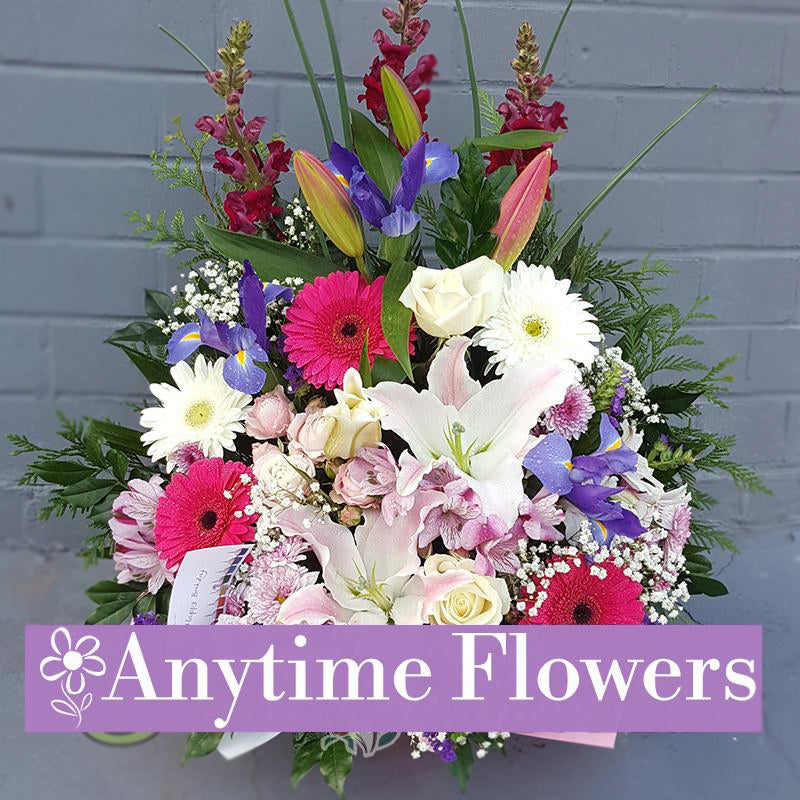 A colourful bouquet of gerberas, irises, lilies, and roses with lush greenery.