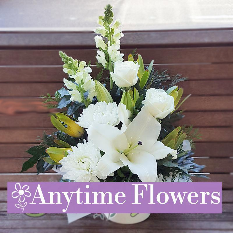 A refined arrangement of white lilies, roses, and snapdragons with lush greenery.