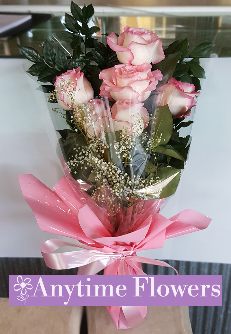 A romantic bouquet of soft pink roses, baby's breath, and lush greenery tied with a pink ribbon.