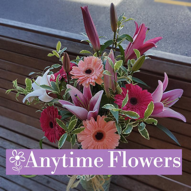 A graceful arrangement of pink lilies, pink gerberas, and vibrant greenery in a clear vase.