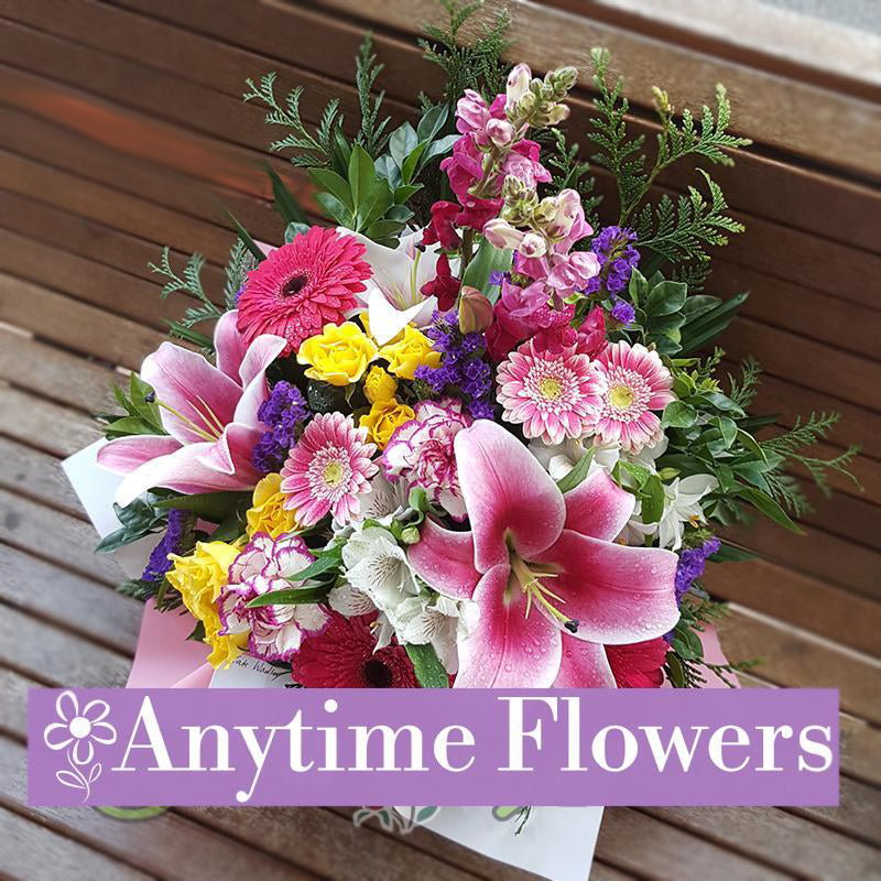 A vibrant bouquet featuring pink lilies, yellow roses, gerberas, and snapdragons with lush greenery.