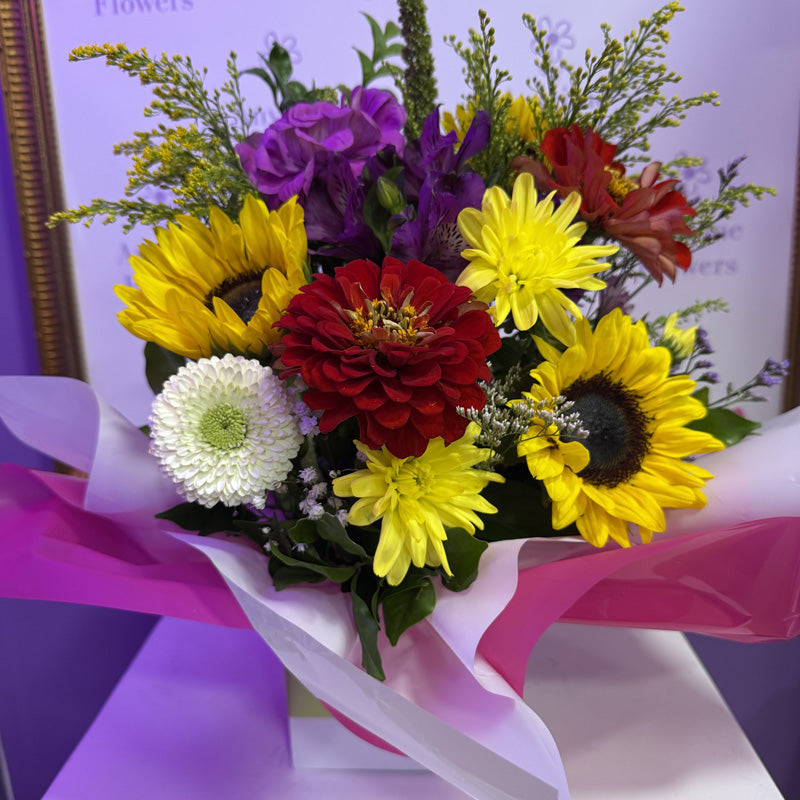 A vibrant mini-box floral arrangement featuring bright sunflowers, yellow daisies, and lush greenery, perfect for bringing sunshine into any room.