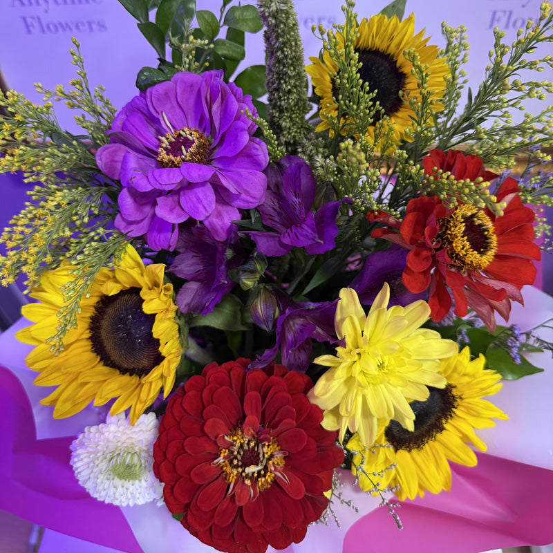 A bright and cheerful floral arrangement in a mini-box, featuring sunflowers, zinnias, and other colorful blooms, perfect for a joyful gift.