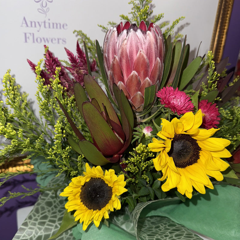 A vibrant native flower arrangement in a mini-box, including proteas, sunflowers, and colorful blooms, ideal for a unique gift.