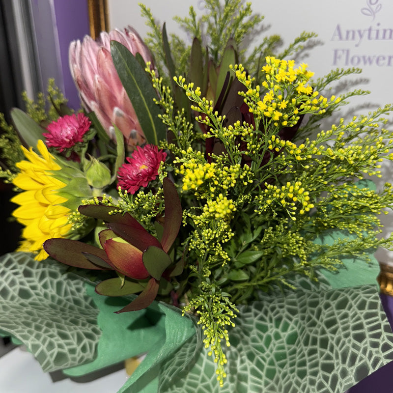 A close-up of a native flower mini-box featuring proteas, sunflowers, and lush greenery for a fresh, nature-inspired display.
