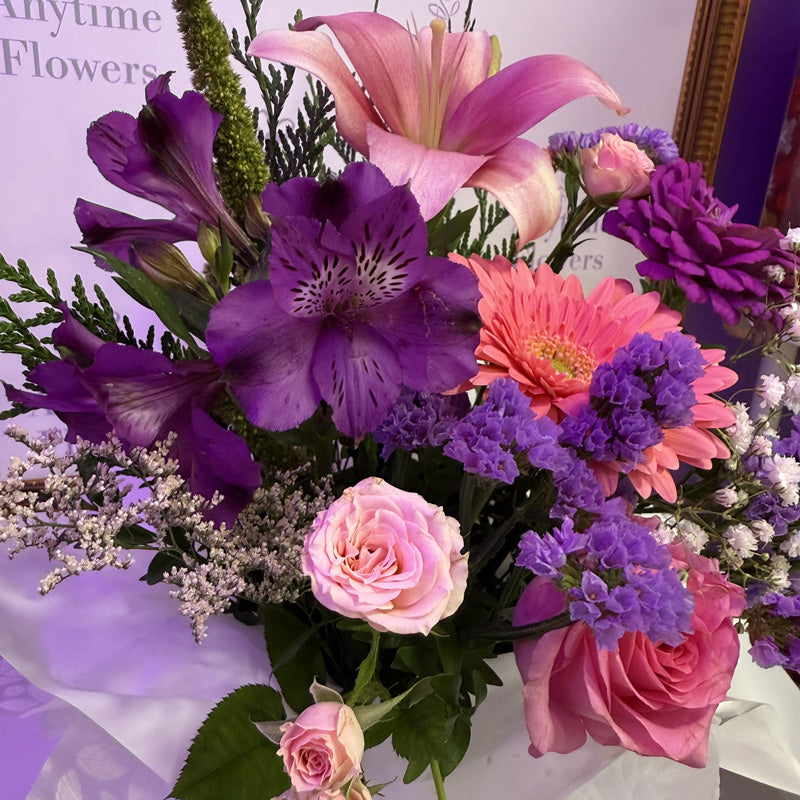 A vibrant mini-box with pink lilies, purple chrysanthemums, and soft pink roses, creating a colorful and elegant display.