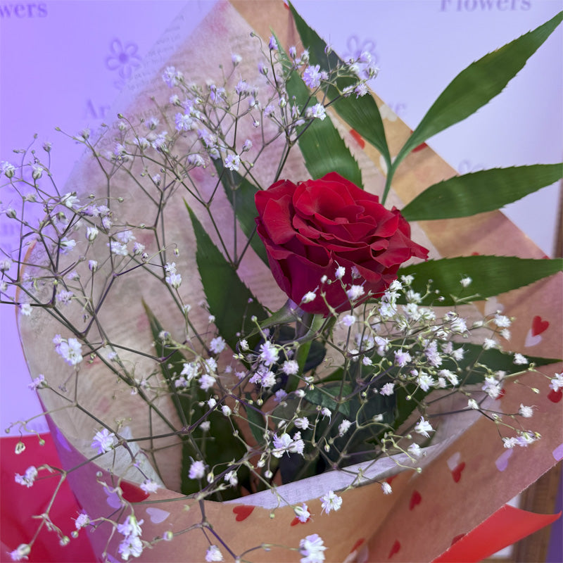 A sophisticated rose arrangement in a bouquet, featuring a single long stemmed fresh red rose for a romantic gesture.