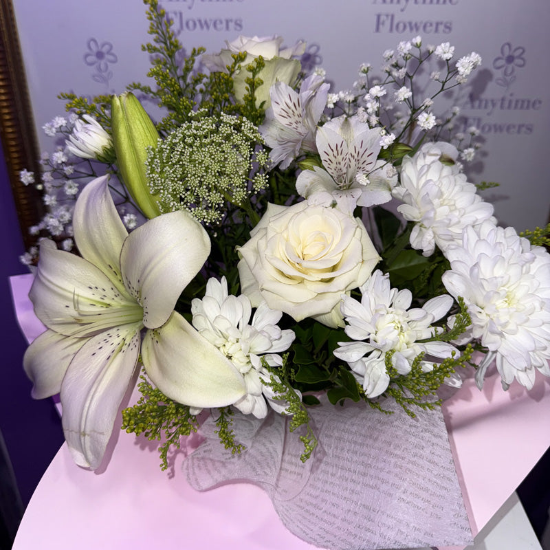 A bouquet of white lilies, roses, chrysanthemums, and gypsophila flowers arranged in a white gift box.