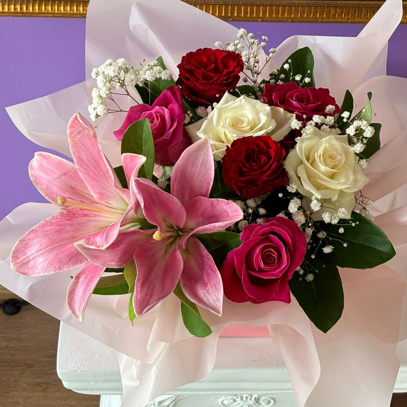 A close-up of the Lily & Rose Delight Box, showcasing pink oriental lilies, red and white roses, and lush greenery in an elegant pink gift box.