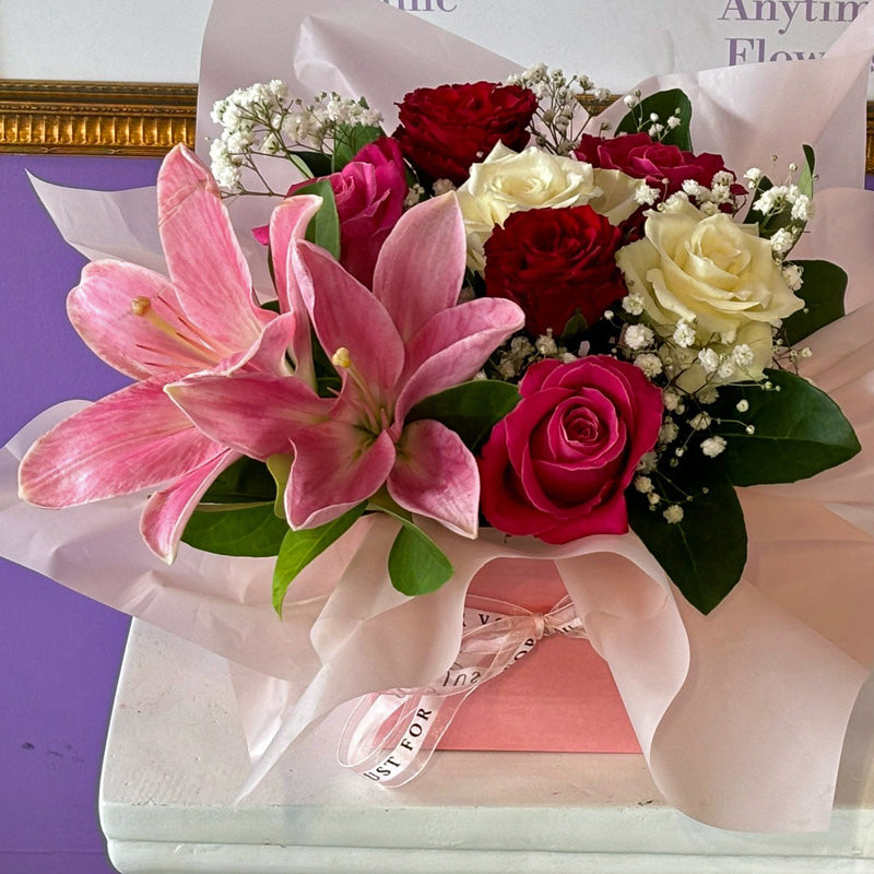 A stunning floral display of fresh pink lilies, velvety roses, and delicate baby's breath, presented in a chic pink box for a romantic touch.