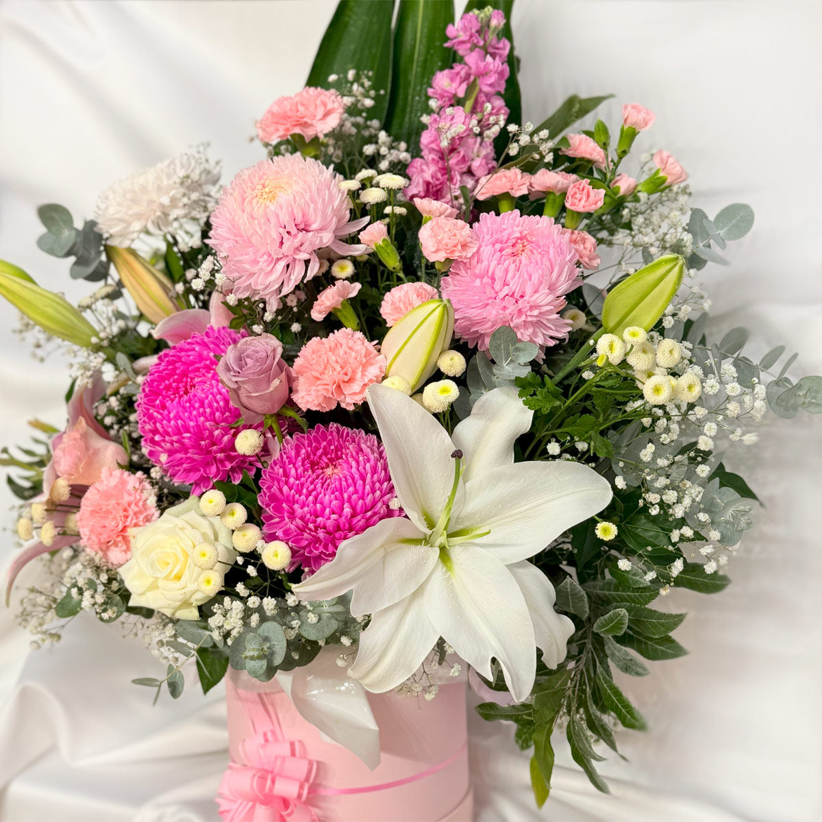 Roses, chrysanthemums and lilies in a pink flower arrangement in a pink hatbox