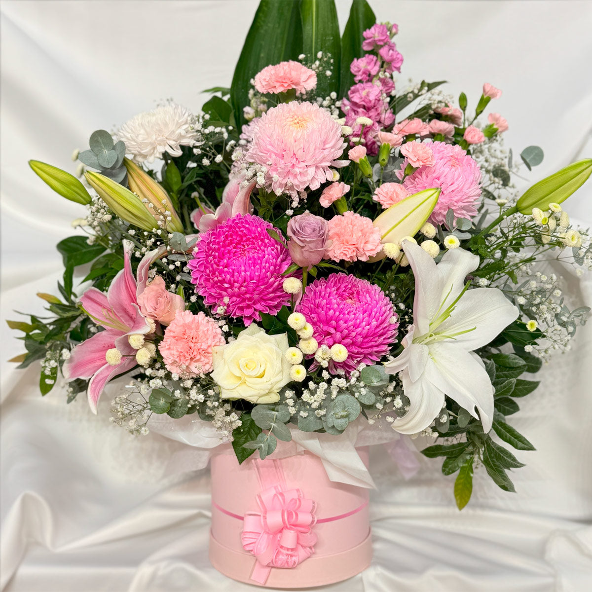 Chrysanthemums, lilies, carnations and roses in a pink hatbox